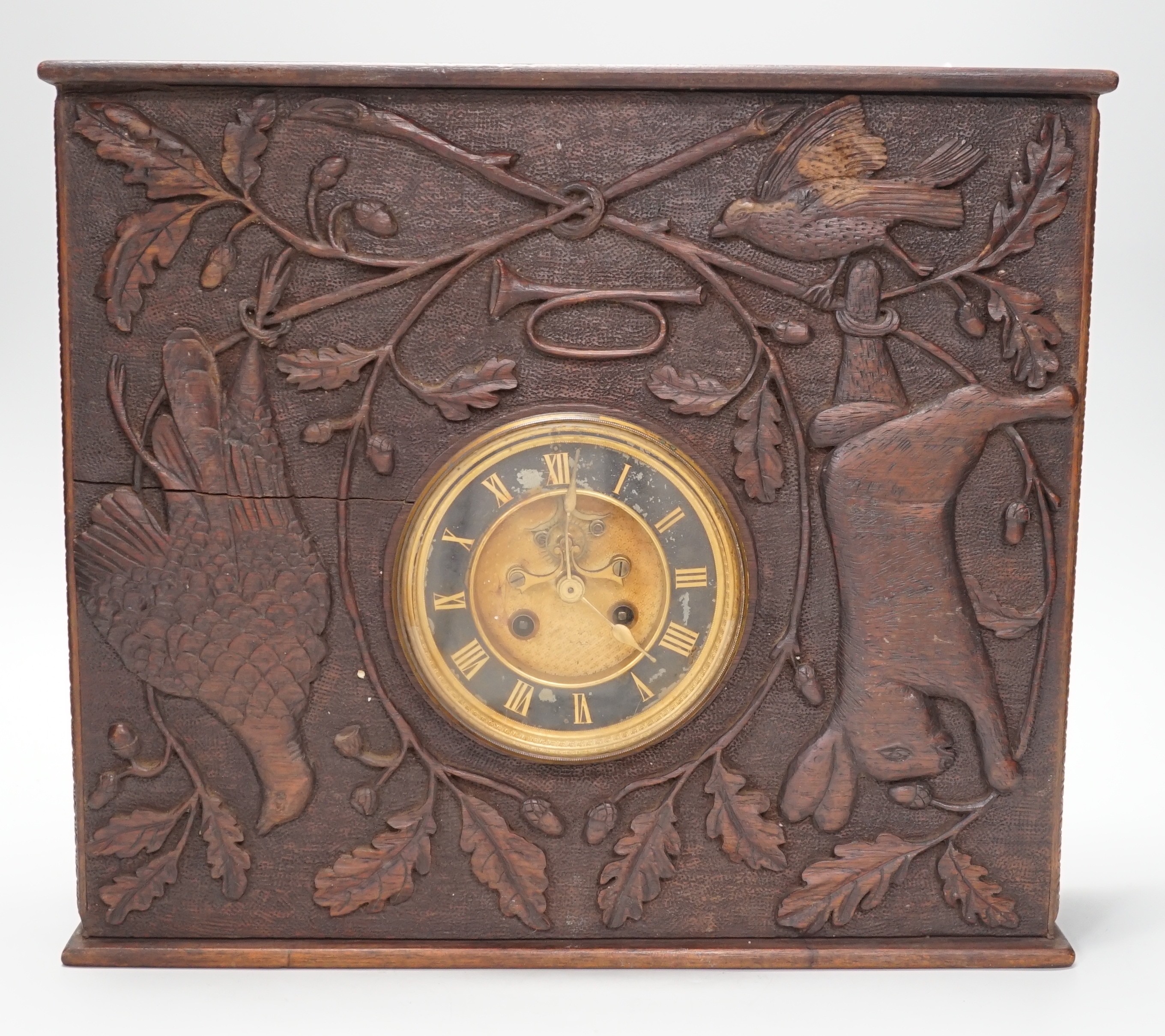 A late 19th century / early 20th century folk art carved oak cased clock, decorated with hanging dead game amongst oak sprigs and acorns, 34x39cm